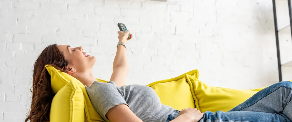 attractive-young-woman-relaxing-under-air-conditioner-and-holding-remote-control